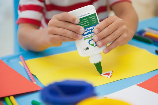 Child applying glue to colorful paper with a bottle of BioBond School Adhesive that is better than glue.