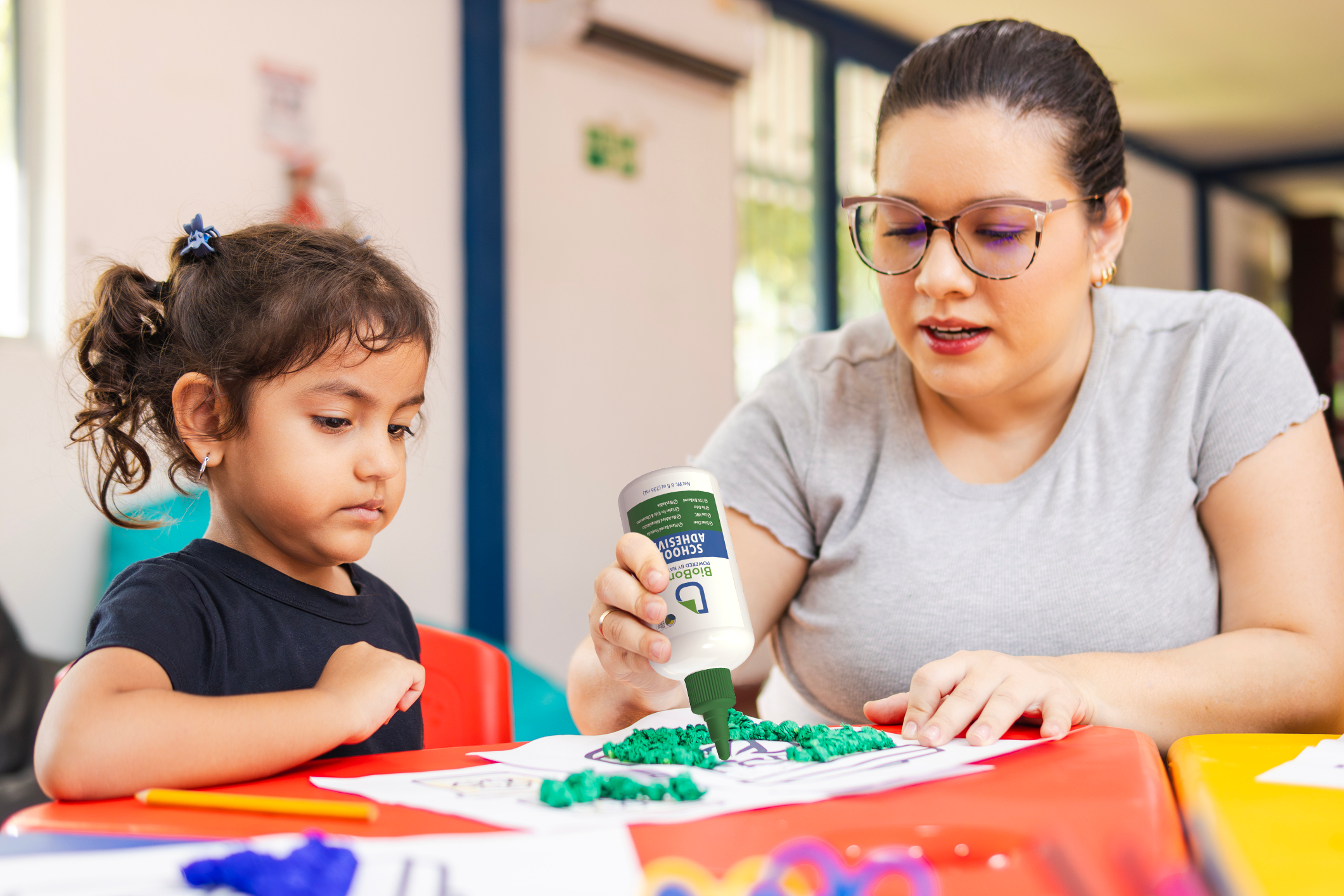 Teacher and child engaged in an activity with BioBond School Glue at a table. 